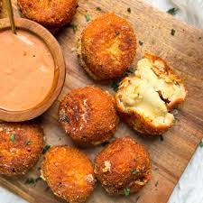 
Crispy golden arancini rice balls stacked on a platter, one cut open to reveal a savory filling, garnished with herbs, served with salt on a wooden table, perfect for Italian cuisine lovers.