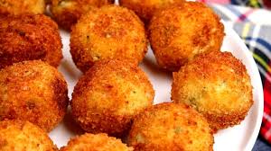 
Crispy golden arancini rice balls stacked on a platter, one cut open to reveal a savory filling, garnished with herbs, served with salt on a wooden table, perfect for Italian cuisine lovers.