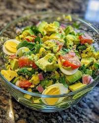 Fresh cucumber, cherry tomato, red onion, and avocado salad in a white bowl, garnished with herbs, showcasing vibrant colors and healthy ingredients, perfect for a nutritious meal.