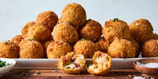 
Crispy golden arancini rice balls stacked on a platter, one cut open to reveal a savory filling, garnished with herbs, served with salt on a wooden table, perfect for Italian cuisine lovers.